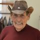 Elderly man in cowboy hat smiling indoors