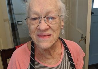 Elderly woman wearing glasses and apron indoors