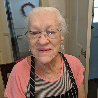 Elderly woman wearing glasses and apron indoors