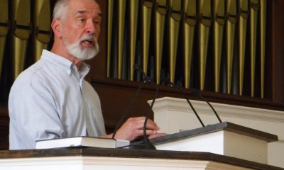 Man speaking at church podium with organ pipes