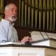 Man speaking at church podium with organ pipes