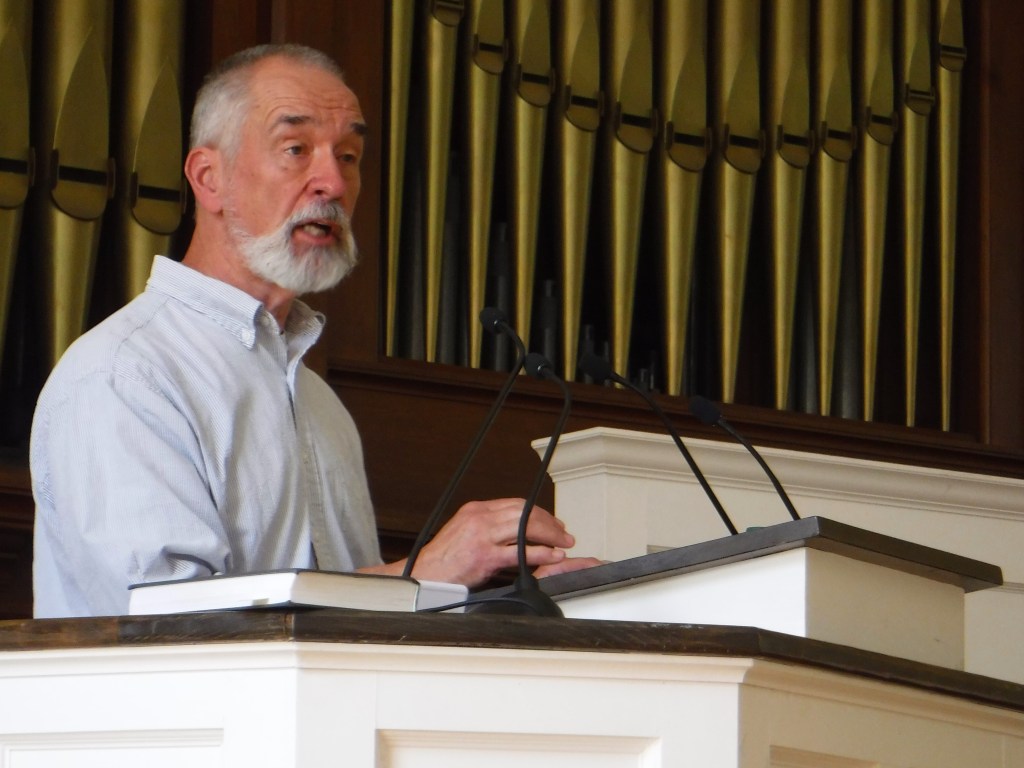 Man speaking at church podium with organ pipes