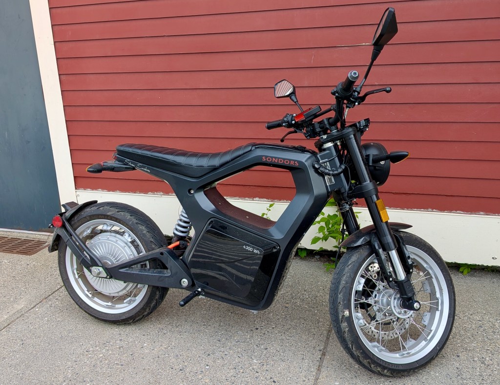 Black SONDORS electric motorcycle parked by red wall