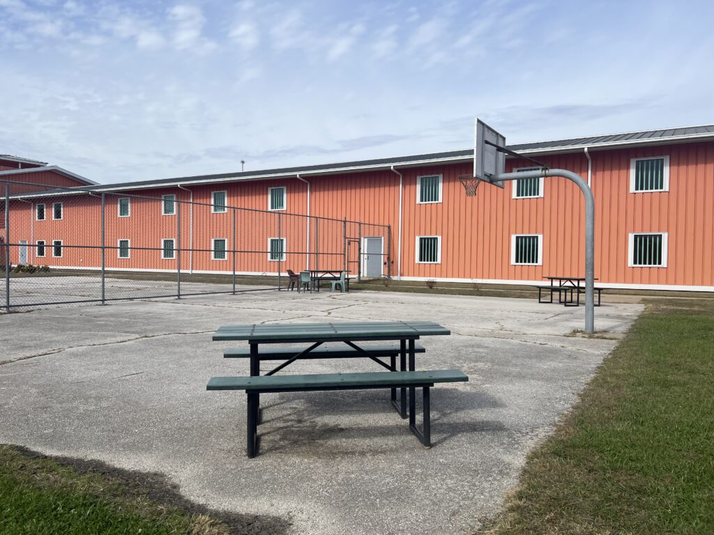 Fenced outdoor yard with picnic tables and basketball hoop