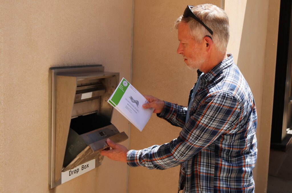 Man placing envelope into ballot drop box
