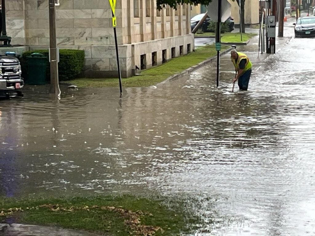 Worker clearing drain in flooded city street