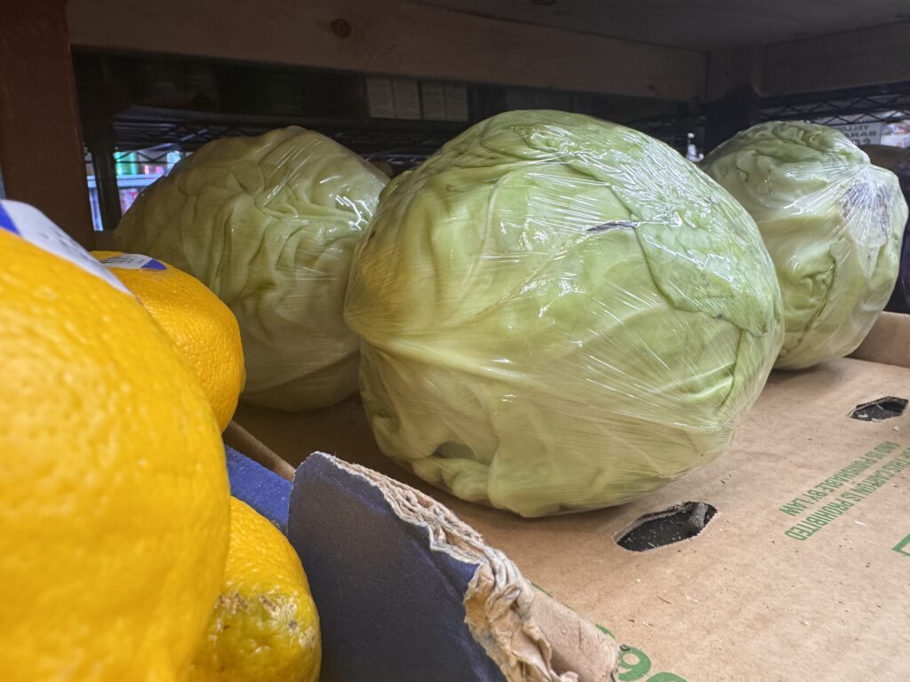 Plastic-wrapped cabbages on store shelf with lemons
