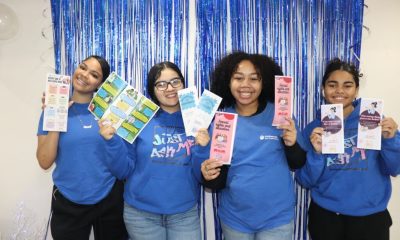 Four women holding educational pamphlets before blue backdrop
