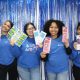 Four women holding educational pamphlets before blue backdrop