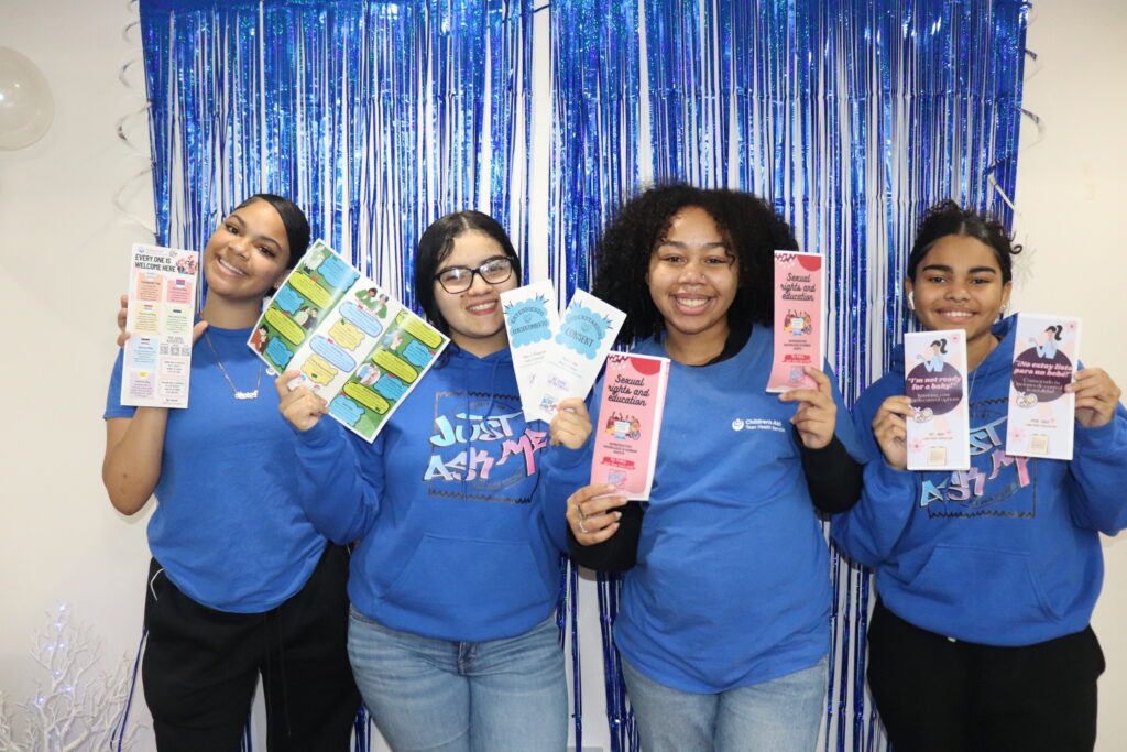 Four women holding educational pamphlets before blue backdrop
