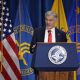 Man speaking at podium with U.S. flags