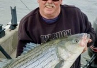 Man holding large striped bass on boat