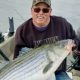 Man holding large striped bass on boat