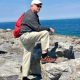 Man with red backpack on rocky coast