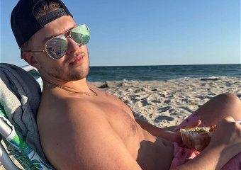 Man relaxing shirtless on beach with sandwich