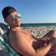 Man relaxing shirtless on beach with sandwich