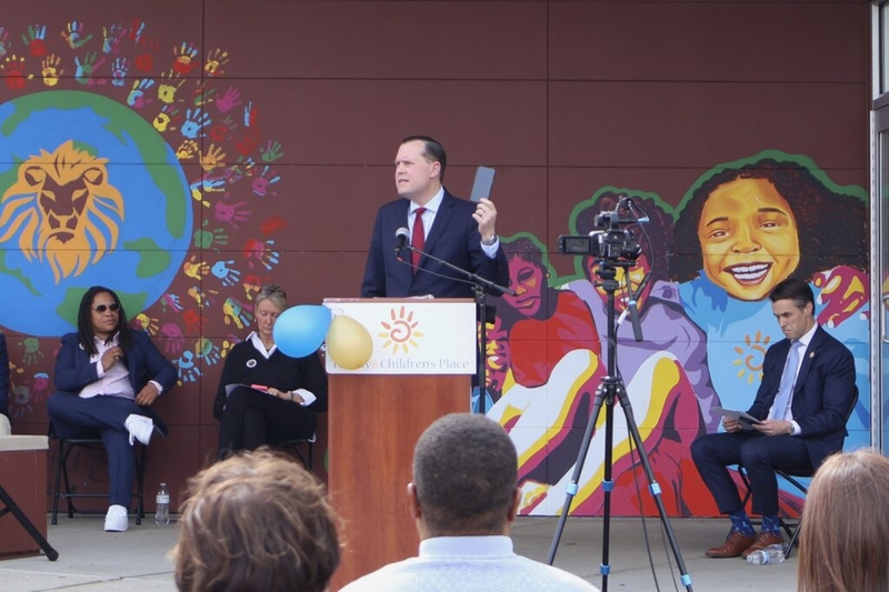 Man speaking at podium before colorful mural