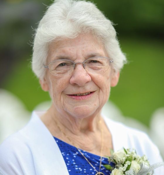 Elderly woman smiling outdoors with white corsage