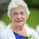 Elderly woman smiling outdoors with white corsage