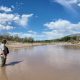 Man standing in shallow muddy river under blue sky