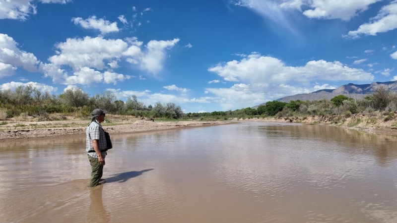 Man standing in shallow muddy river under blue sky