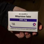 A hand holding a box of mifepristone tablets, labeled 200 mg, emphasizing the medication's i — mifepristone lawsuit paused