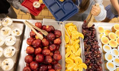 A school cafeteria table filled with fresh fruits like apples, oranges, and grapes, alongsid — SNAP cuts free school lunch
