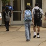 Students walking towards a school entrance, carrying backpacks, highlighting the issue of school closures and consolidations.
