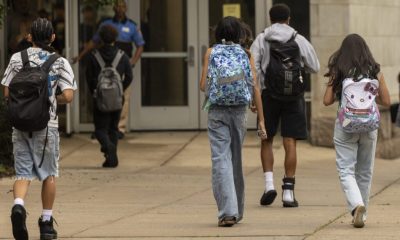 Students walking towards a school entrance, carrying backpacks, highlighting the issue of school closures and consolidations.