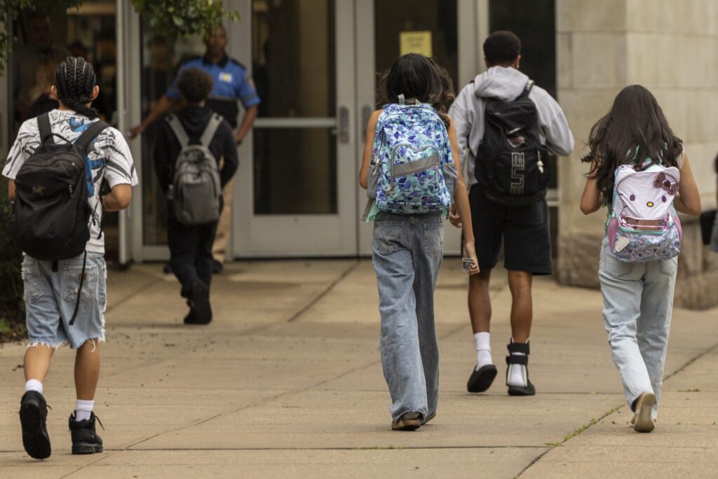 Students walking towards a school entrance, carrying backpacks, highlighting the issue of school closures and consolidations.
