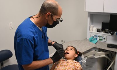 A dentist examining a young girl in a dental office, highlighting immigrant children missing healthcare.