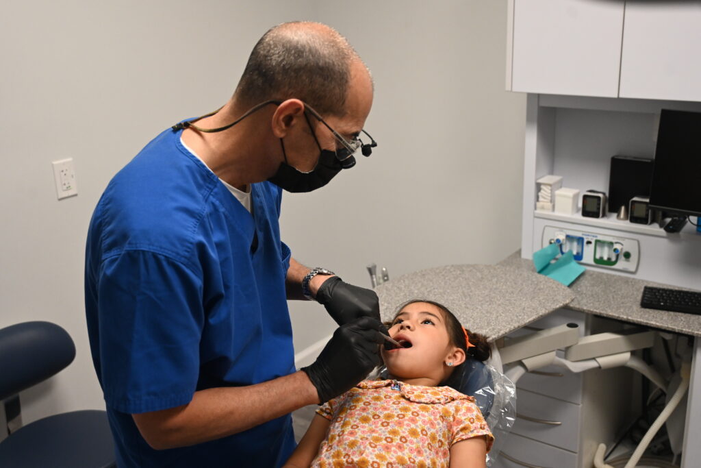A dentist examining a young girl in a dental office, highlighting immigrant children missing healthcare.
