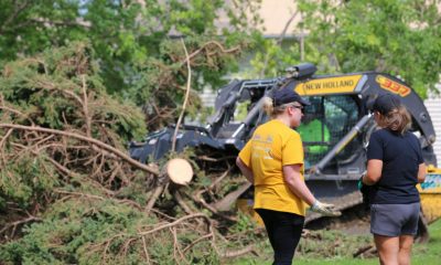 Two women discuss cleanup efforts near a tree debris pile and a construction vehicle after a storm, hi — FEMA disaster aid