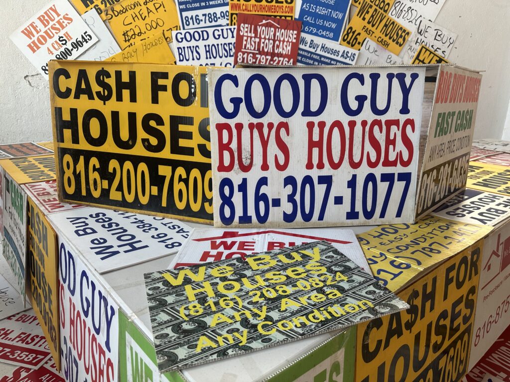 Colorful signs advertising cash offers for homes, featuring phone numbers and phrase — real estate wholesaling regulations