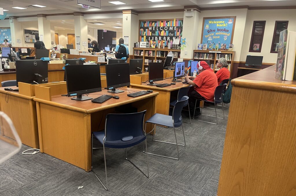 Library interior with computers, students using them, and a welcome sign on the wall, highlighting E-Rate program funding…