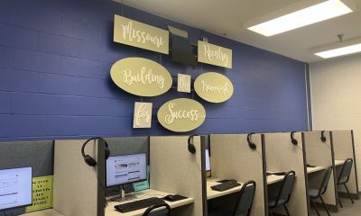 A room with cubicles containing computers and headsets, featuring a wall sign — women on parole mental health and housing
