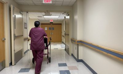 A healthcare worker in scrubs pushing a patient in a walker down a hospital corridor. — Medicaid Provider Payment Cuts