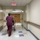 A healthcare worker in scrubs pushing a patient in a walker down a hospital corridor. — Medicaid Provider Payment Cuts