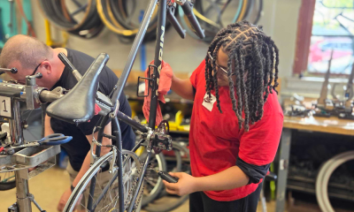 A young person in a red shirt adjusts a bicycle in a workshop with bike tires in th — upstate new york bike infrastructure