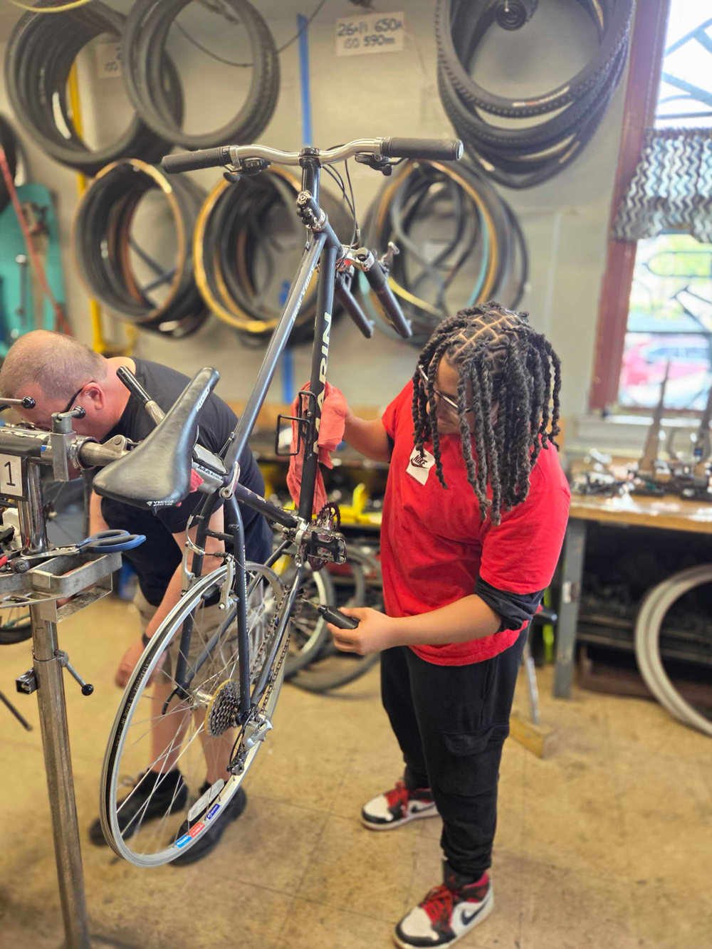 A young person in a red shirt adjusts a bicycle in a workshop with bike tires in th — upstate new york bike infrastructure