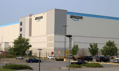 Amazon warehouse building with logo, surrounded by parking lot and trees, under a clear s — FTC Amazon advertising lawsuit