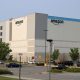 Amazon warehouse building with logo, surrounded by parking lot and trees, under a clear s — FTC Amazon advertising lawsuit