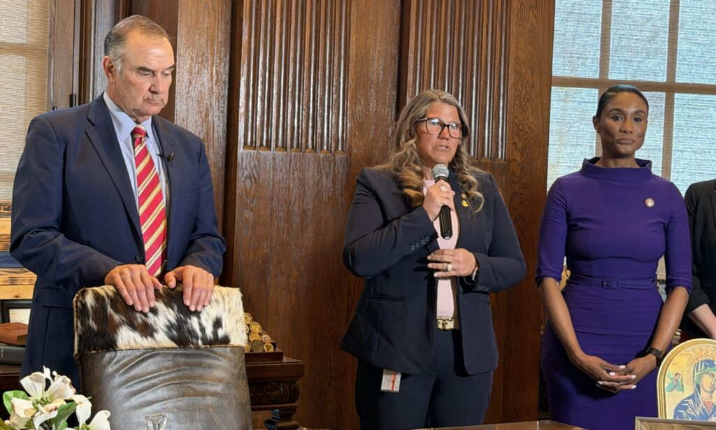 Three individuals stand in a formal setting discussing no-fault divorce laws, with one speaking into a microphone.
