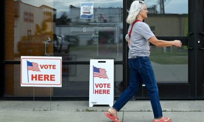 A woman walks past polling place signs indicating voting is available, with American fl — federal troops at polling places