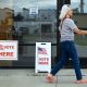 A woman walks past polling place signs indicating voting is available, with American fl — federal troops at polling places