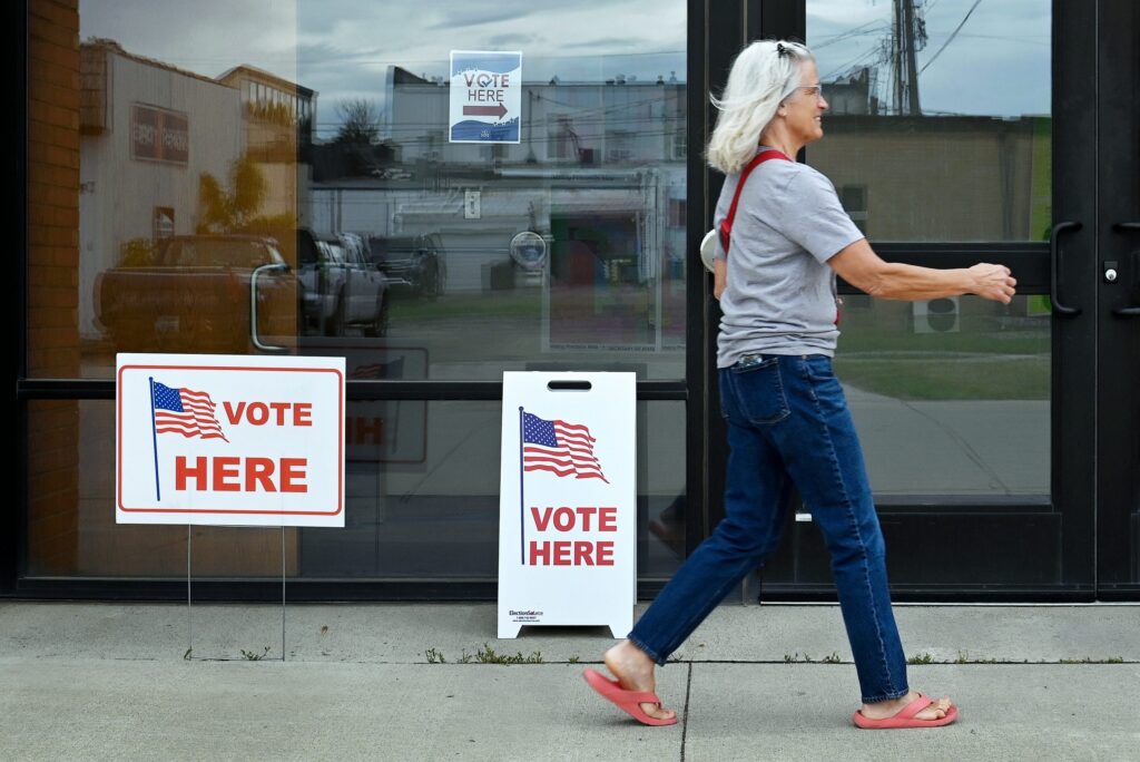 A woman walks past polling place signs indicating voting is available, with American fl — federal troops at polling places