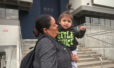 A woman holding a young child outside a building, both smiling, with the number 66 — trump green card restrictions lawsuit