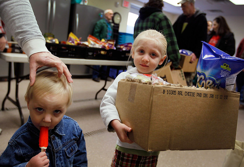 Two children at a food distribution event, one holding a box of snacks and the other with a — US poverty rate census data