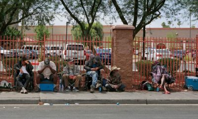People sitting along sidewalk beside red fence — Escambia County homelessness laws