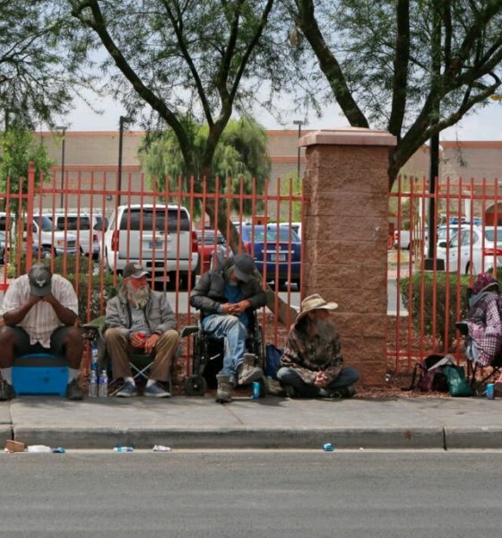 People sitting along sidewalk beside red fence — Escambia County homelessness laws